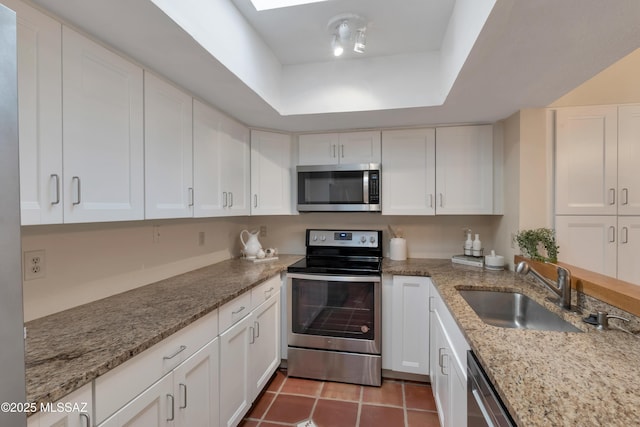 kitchen with appliances with stainless steel finishes, a raised ceiling, white cabinets, and a sink