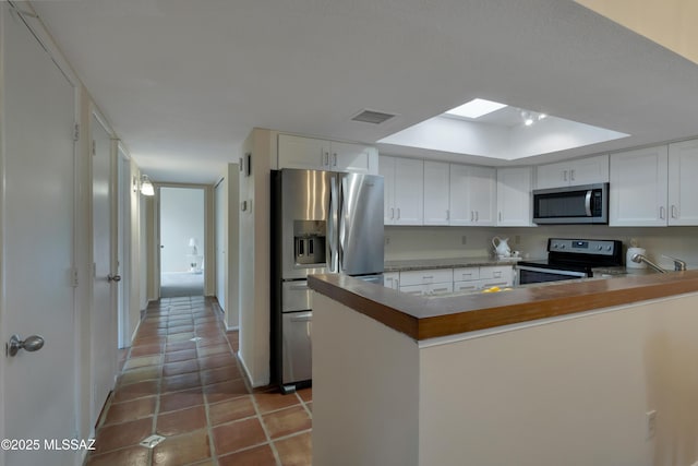 kitchen with a peninsula, white cabinetry, visible vents, and stainless steel appliances