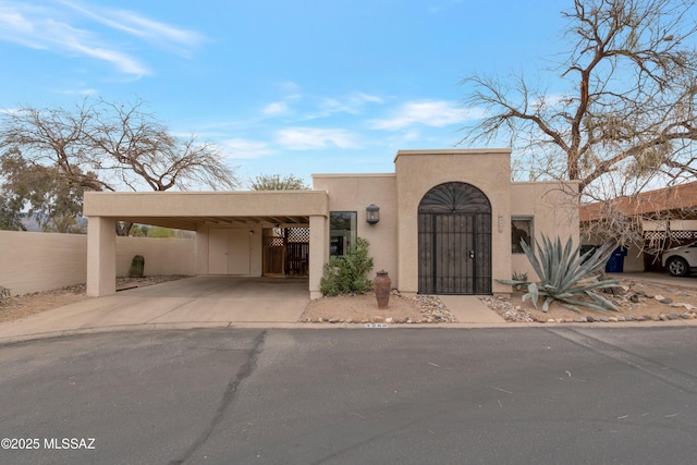 pueblo revival-style home featuring a gate, fence, concrete driveway, and stucco siding