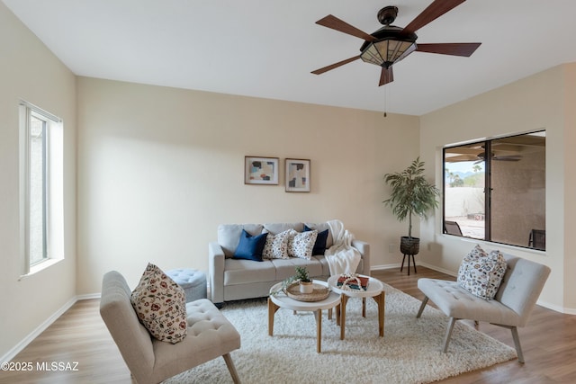 living room featuring baseboards, a ceiling fan, light wood-style flooring, and a healthy amount of sunlight