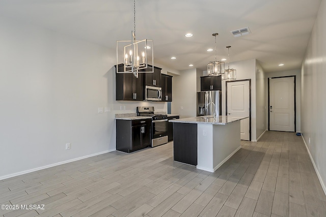 kitchen with stainless steel appliances, visible vents, hanging light fixtures, light wood-style flooring, and baseboards