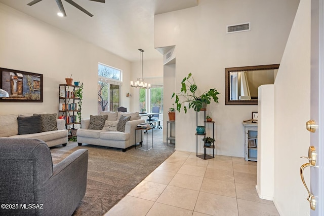 living area featuring light tile patterned floors, ceiling fan with notable chandelier, visible vents, and baseboards