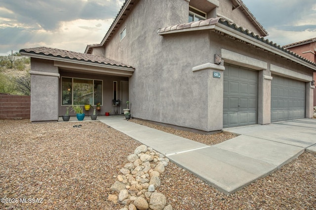 view of side of home with an attached garage, a tiled roof, and stucco siding