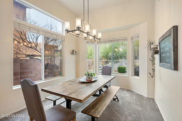 dining area with carpet floors, an inviting chandelier, a towering ceiling, and baseboards