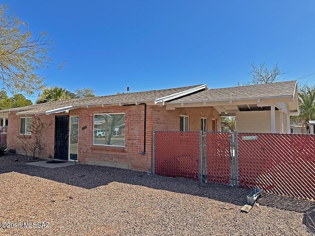 view of front of home with a gate, brick siding, a fenced front yard, and roof with shingles