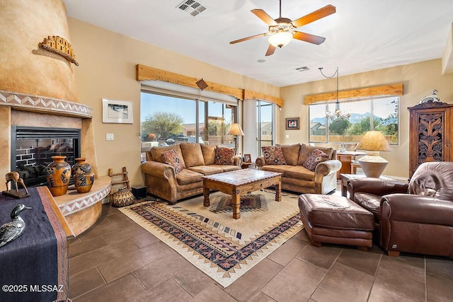 living area featuring a fireplace, visible vents, and ceiling fan with notable chandelier