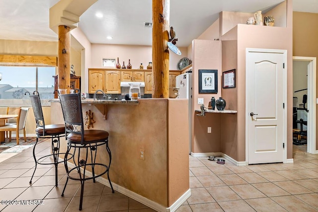 kitchen with baseboards, visible vents, a kitchen breakfast bar, and light tile patterned floors