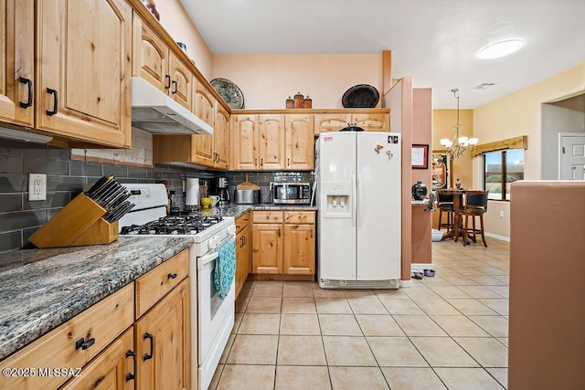 kitchen with light tile patterned flooring, a notable chandelier, under cabinet range hood, white appliances, and backsplash