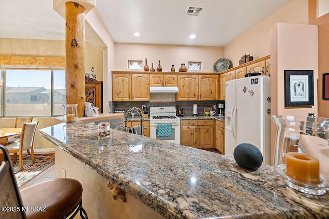 kitchen with stone countertops, under cabinet range hood, white appliances, visible vents, and backsplash