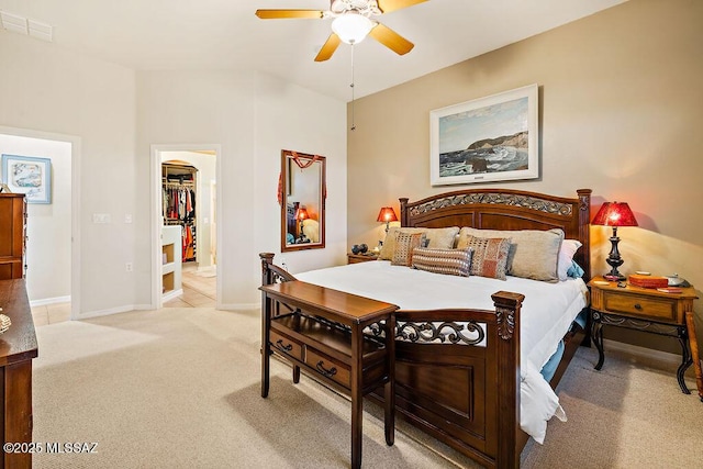 bedroom with a walk in closet, visible vents, a ceiling fan, light carpet, and baseboards