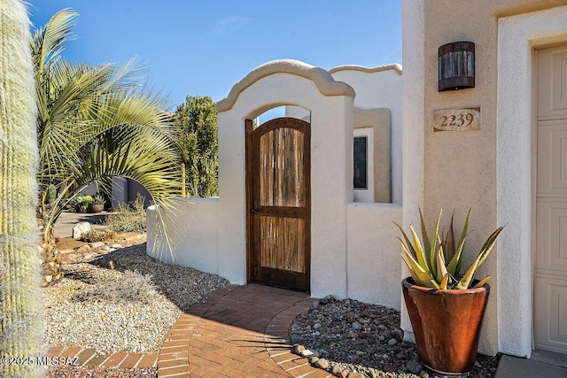 view of exterior entry featuring a gate and stucco siding