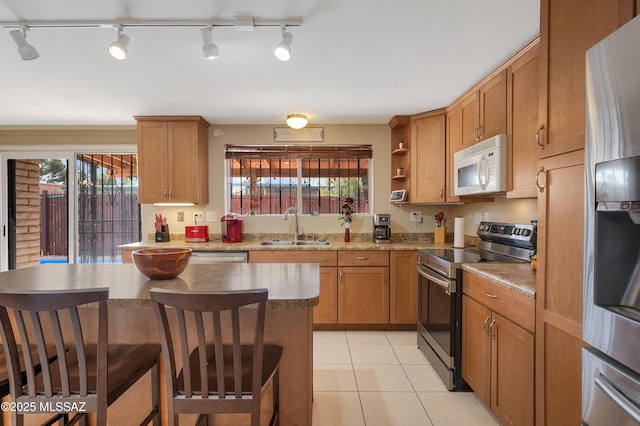 kitchen featuring a breakfast bar area, light tile patterned flooring, a sink, appliances with stainless steel finishes, and brown cabinetry