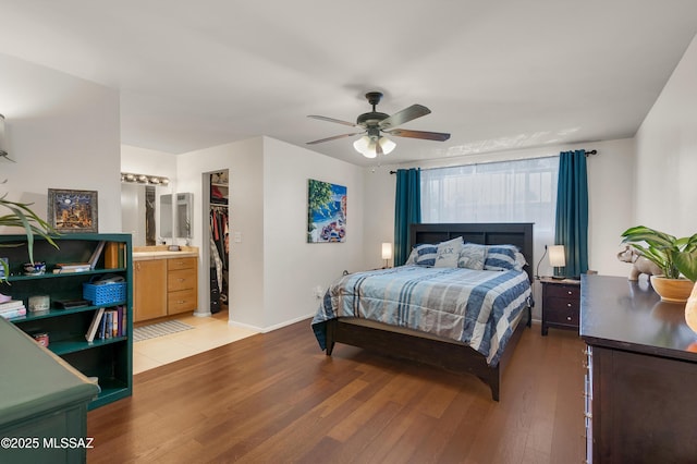 bedroom featuring light wood finished floors, a spacious closet, ensuite bathroom, ceiling fan, and baseboards