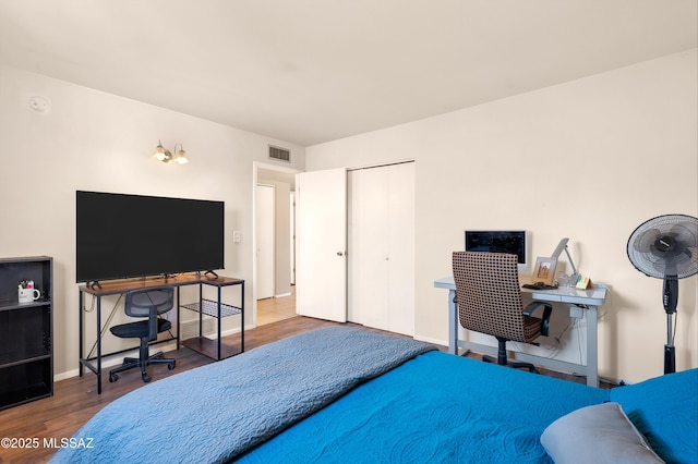 bedroom with a closet, wood finished floors, visible vents, and baseboards