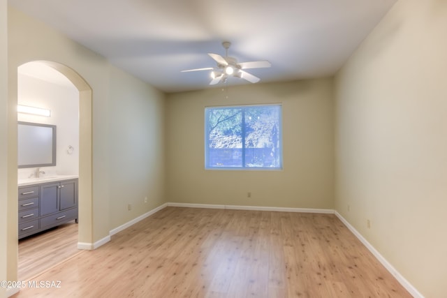 unfurnished bedroom with baseboards, arched walkways, light wood finished floors, and a sink