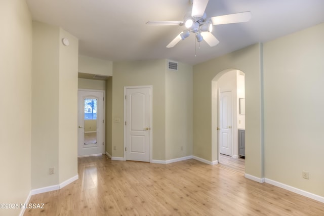 spare room with visible vents, ceiling fan, baseboards, light wood-style floors, and arched walkways