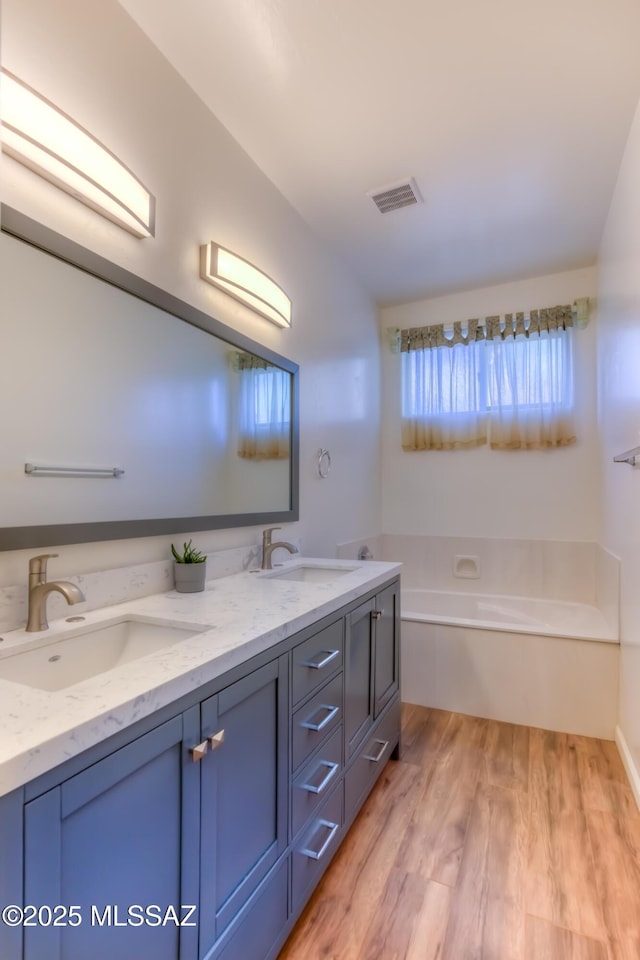 bathroom with visible vents, a garden tub, a sink, wood finished floors, and double vanity