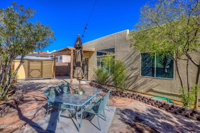 view of patio / terrace featuring a shed, outdoor dining space, an outdoor structure, and fence