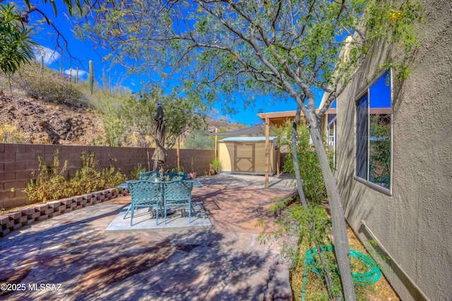 view of patio featuring outdoor dining space, an outdoor structure, a storage unit, and a fenced backyard