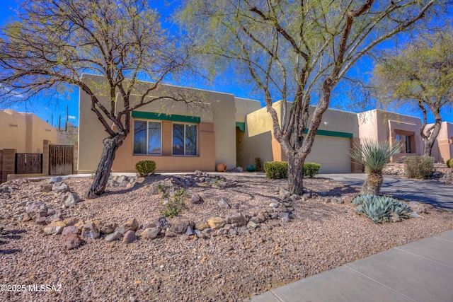 pueblo-style home with a garage, driveway, and stucco siding