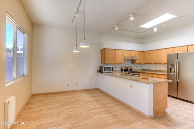 kitchen featuring white microwave, a peninsula, stainless steel fridge with ice dispenser, a sink, and under cabinet range hood