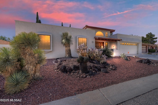 view of front of property with stucco siding, driveway, a tile roof, and a garage