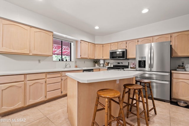 kitchen with light tile patterned floors, light brown cabinetry, light countertops, appliances with stainless steel finishes, and a kitchen bar