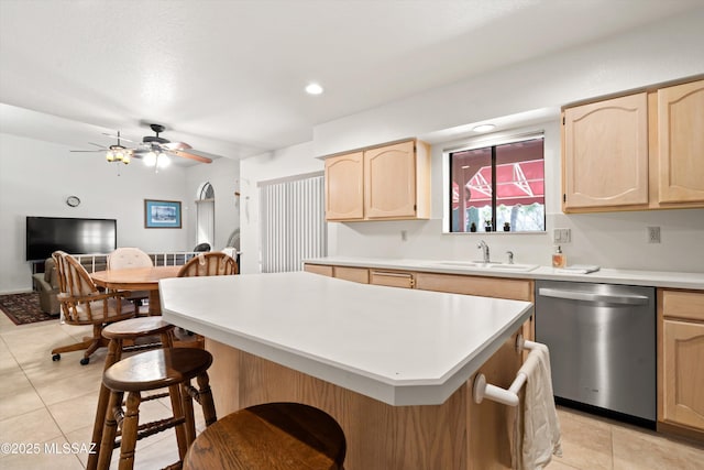 kitchen featuring a center island, light brown cabinetry, a breakfast bar, stainless steel dishwasher, and a sink