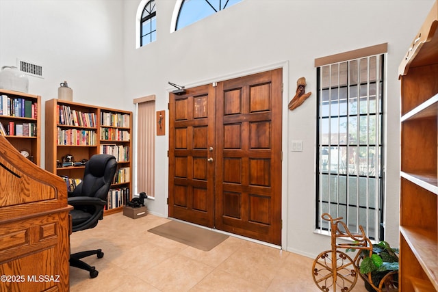 tiled office space featuring visible vents, baseboards, and a towering ceiling