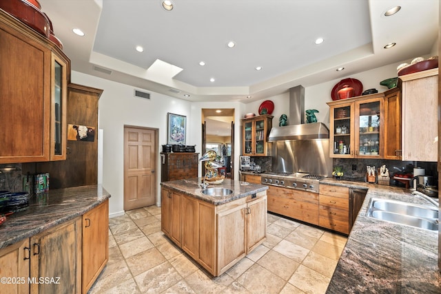 kitchen with wall chimney range hood, stainless steel gas cooktop, a raised ceiling, and a sink