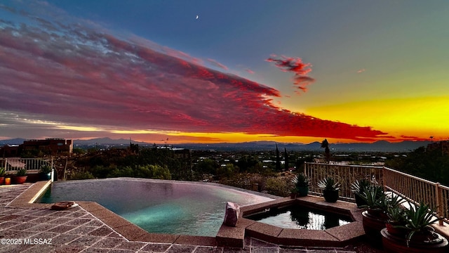 pool at dusk featuring a mountain view and an in ground hot tub