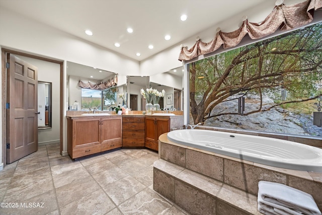 bathroom with a garden tub, double vanity, a sink, and stone tile flooring