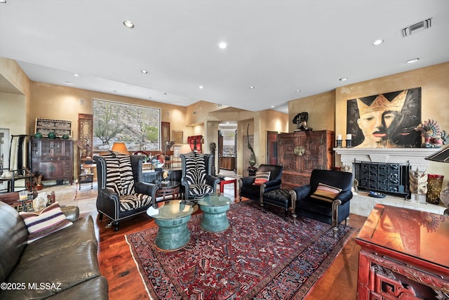 living room with recessed lighting, visible vents, a fireplace with raised hearth, and wood finished floors