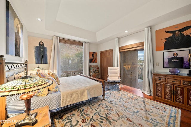 bedroom featuring access to exterior, a raised ceiling, wood finished floors, and recessed lighting