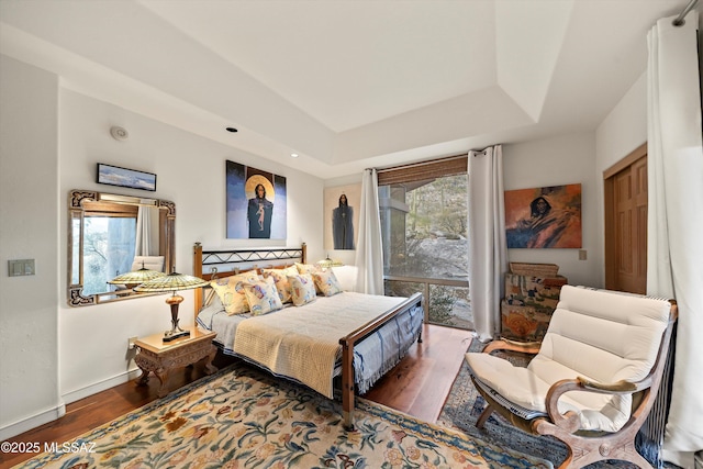 bedroom featuring access to exterior, baseboards, a tray ceiling, and wood finished floors