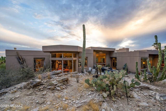 back of house at dusk featuring stucco siding