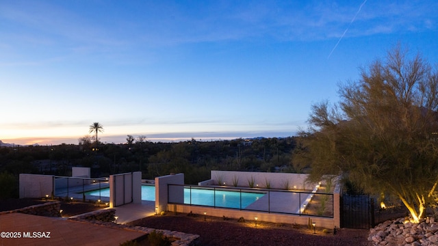 pool at dusk featuring fence and an outdoor pool