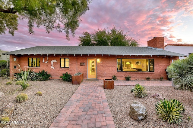 single story home featuring roof with shingles, brick siding, and a chimney