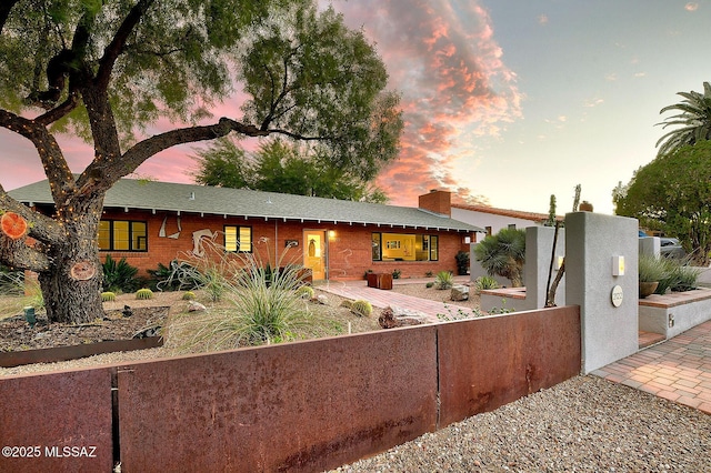 single story home featuring a fenced front yard, a chimney, and brick siding