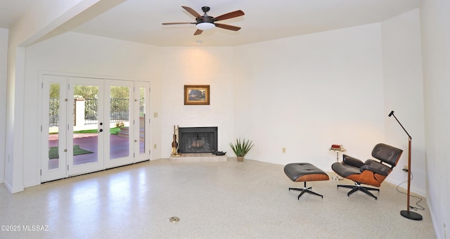 sitting room with french doors, a fireplace with raised hearth, a ceiling fan, and speckled floor