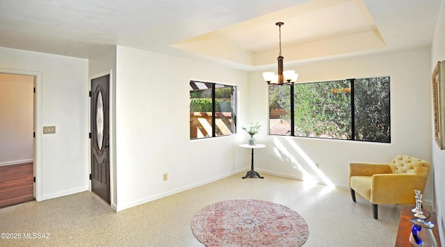 living area featuring a chandelier, a raised ceiling, and baseboards