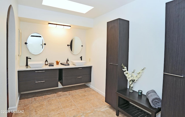 bathroom with a skylight, a sink, baseboards, and double vanity