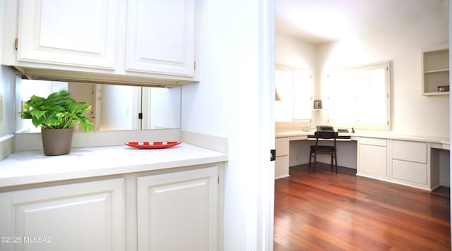 kitchen with light countertops, built in desk, dark wood-type flooring, and white cabinetry