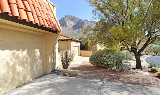 view of property exterior featuring an attached garage, a tile roof, a mountain view, and stucco siding