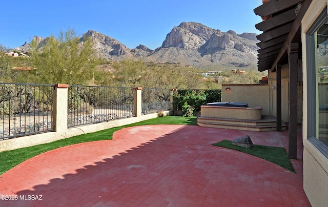 view of patio with a mountain view, a hot tub, and fence