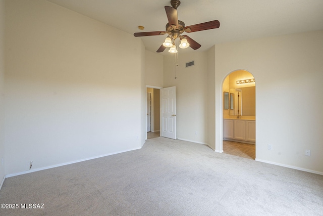 unfurnished bedroom with arched walkways, light colored carpet, visible vents, ensuite bathroom, and baseboards