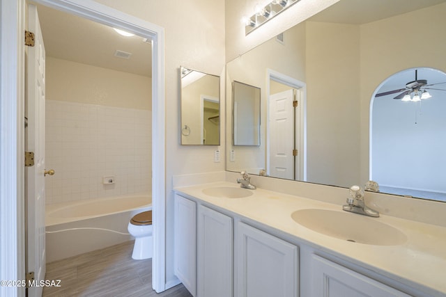 full bath with ceiling fan, a sink, toilet, and double vanity