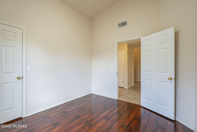 unfurnished room with vaulted ceiling, dark wood-style flooring, visible vents, and baseboards