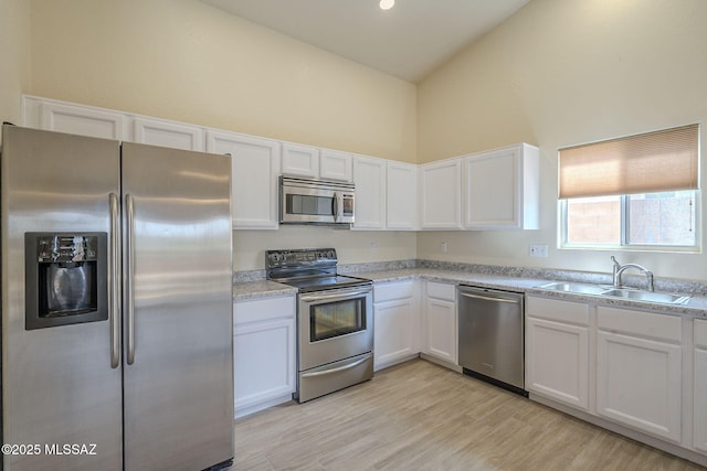 kitchen with stainless steel appliances, a sink, white cabinetry, light countertops, and light wood-type flooring