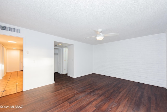 spare room with brick wall, a textured ceiling, visible vents, and wood finished floors